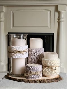 several candles are sitting on a wooden tray in front of a fireplace with white knitted fabric wrapped around them