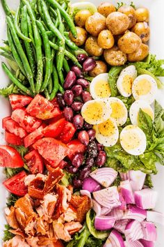 a white platter filled with different types of vegetables and eggs on top of each other