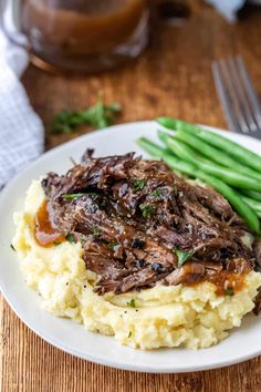 a white plate topped with mashed potatoes covered in meat and gravy next to green beans