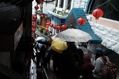 several people are walking down the street with umbrellas in their hand and lanterns hanging above them