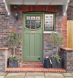 a green front door with two planters and a watering can on the brick walkway