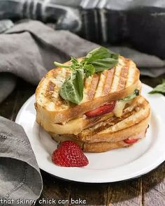 a grilled cheese sandwich on a plate with strawberries and basil leaf garnish