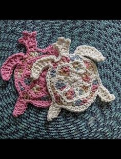 two crocheted turtles on top of a blue mat with pink and white trim