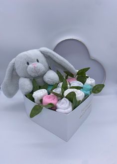 a stuffed bunny sitting in a box filled with baby blankets and greenery on a white background