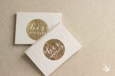 two coasters with gold foil on them sitting on top of a beige tablecloth