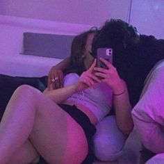 two people sitting on a couch looking at their cell phones while one person takes a selfie