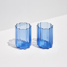 two blue glass vases sitting on top of a white table next to each other