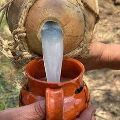 a person holding an orange cup with water coming out of it and pouring from the top