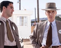 two men in suits and ties standing next to each other, one wearing a hat