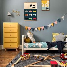 a child's bedroom decorated in blue, yellow and grey with toys on the floor