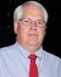 an older man with glasses and a red tie is looking at the camera while standing in front of a dark background