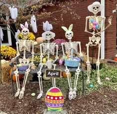 skeleton decorations are displayed in front of a brick building with flowers and bunnies on the ground