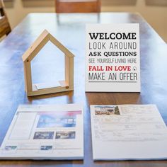 an open house sign sitting on top of a table next to a small wooden house