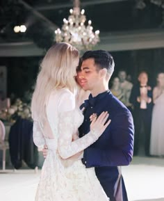 a man and woman standing next to each other in front of a chandelier