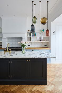 a kitchen with marble counter tops and black cabinets, hanging lights over the island area