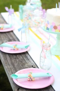 a table topped with pink plates covered in cake next to a jar filled with candles