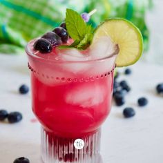 a close up of a drink on a table with blueberries and limes around it