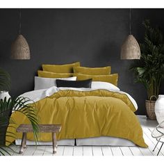 a bed with yellow and white comforters in a room next to potted plants