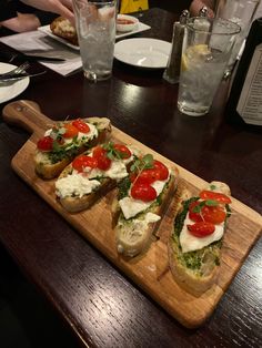 three slices of bread with tomatoes, cheese and spinach on them sitting on a wooden cutting board