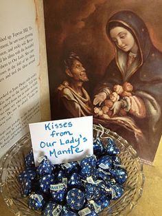 a glass bowl filled with blue chocolates next to an open book on a table