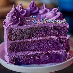 a slice of cake with purple frosting and sprinkles sits on a plate