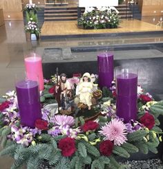 purple candles are sitting on top of a table with flowers and greenery in front of it