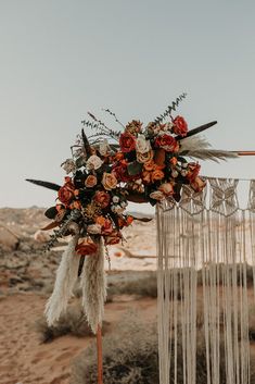 a wedding arch decorated with flowers and feathers for an outdoor ceremony in the desert at sunset