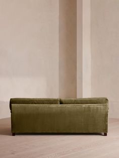 a green couch sitting on top of a hard wood floor next to a white wall