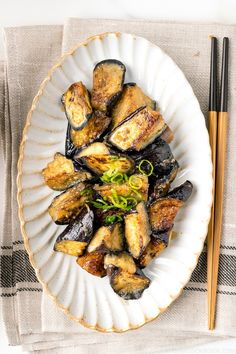 a white plate topped with fried eggplant and chopsticks next to a fork