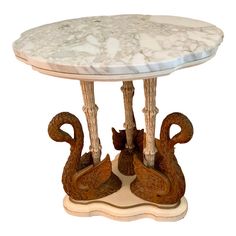 a marble topped table with two swans on the base and one swan sitting under it