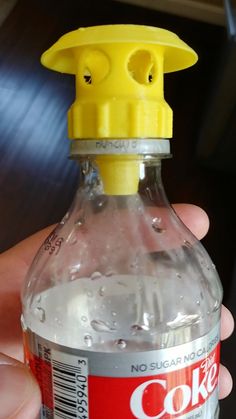 a hand holding a plastic bottle with water in it's mouth and a yellow cap on the top