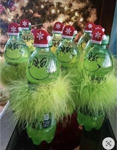 some green water bottles with hats on them and fuzzy fur around the edges, sitting in front of a christmas tree