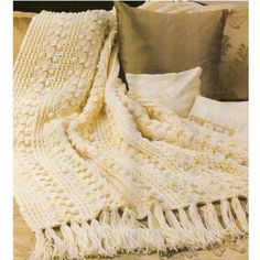 a white crocheted blanket sitting on top of a bed next to pillows and blankets