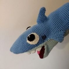 a crocheted stuffed shark head hanging on the wall with it's mouth open