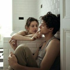 a man and woman sitting on the floor in a bathroom looking at each other's eyes