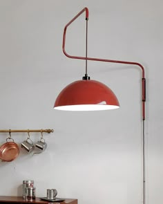 a red lamp hanging from the ceiling over a table with pots and pans on it