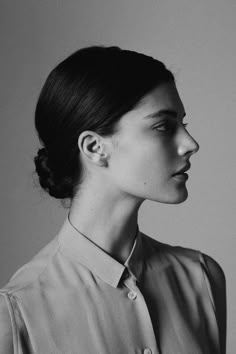 a black and white photo of a woman wearing a shirt with her hair in a bun