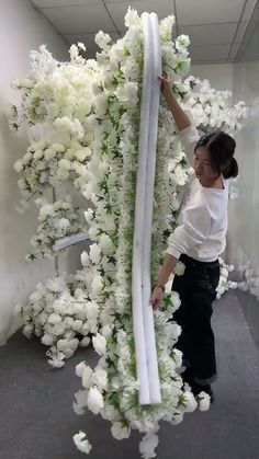 a woman standing next to a tall white flower covered wall in an office building with flowers all over the floor