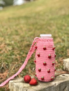 a pink crocheted water bottle cover with strawberries on the side sitting on a piece of wood