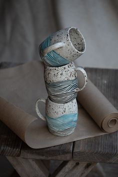 three ceramic mugs stacked on top of each other next to a rolled up piece of paper