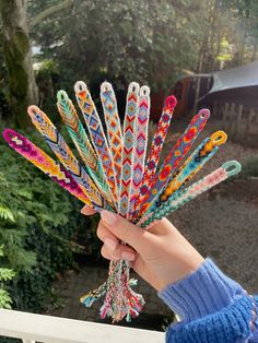 a person holding up a bunch of colorful crochet hooks in front of a house