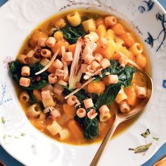 a bowl of pasta and spinach soup with a spoon on a blue and white plate