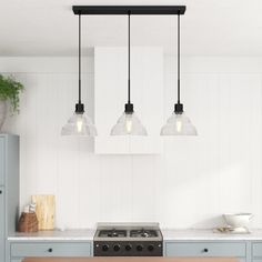 three lights hanging over a stove top oven in a kitchen with blue cabinets and white walls