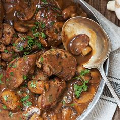 meat and mushroom stew with gravy in a pan on a table next to garlic