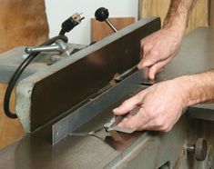 a man working on a piece of metal with a machine in his hand and some woodworking tools next to him