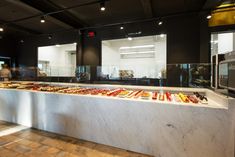 a counter with lots of different types of food on it in a room filled with people