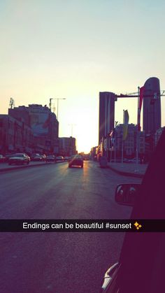 the sun is setting on an empty street with cars driving down it and buildings in the background