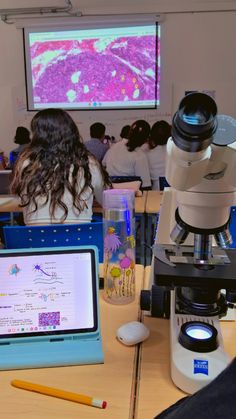 two people sitting at a table with microscopes in front of them, looking into a computer screen