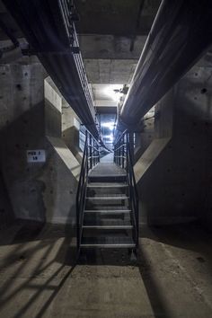 some stairs going up and down in a dark room with light coming from the ceiling