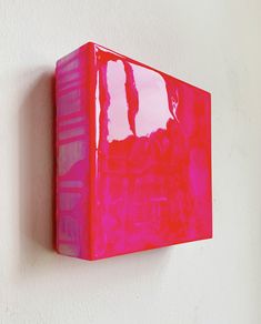 a red box hanging on the wall with pink paint overlaying it's surface